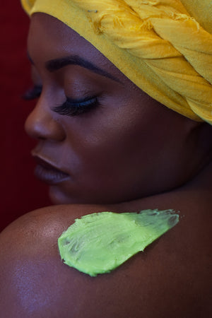 Model with long eyelashes in Bright yellow headwrap with a schmear of our green colored Fresh Garden Apple Body Butter on her shoulder